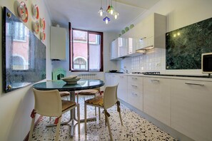A modern kitchen with white cabinets, a marble countertop, and a dining area with a glass table and chairs. - REMIGIO Marco-canal (Venice)