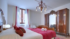 Ett hotellrum med en stor säng, en garderob i trä, en kristallkrona och ett fönster med gardiner.