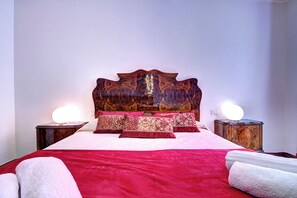 A neatly made bed with a red bedspread, multiple pillows, and two bedside tables with lamps. - REMIGIO Marco-canal (Venice)
