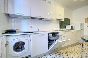 A modern kitchen with white cabinetry, a built-in dishwasher, a washing machine, and a microwave. - REMIGIO Marco-canal (Venice)