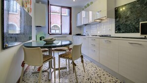 Ett modernt kök med vita skåp, en bänkskiva i marmor och en matplats med ett glasbord och stolar.