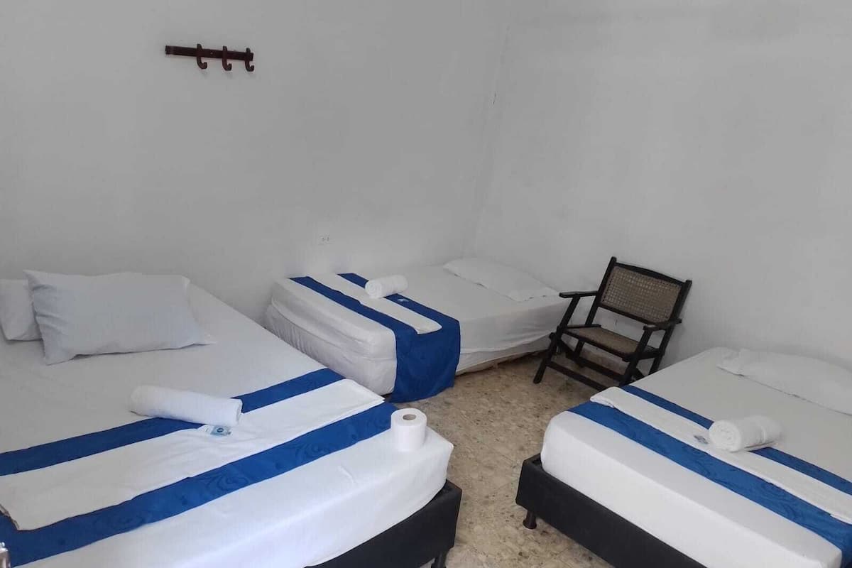A room with three beds, each with white and blue striped bedding, a chair, and a wall-mounted hook.