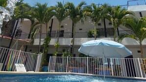 Una piscina con agua azul cristalina, rodeada de palmeras y un edificio con balcones.