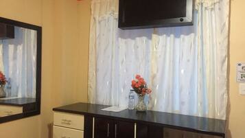 A bedroom with a bed, a dresser, a TV mounted on the wall, and a window with curtains.
