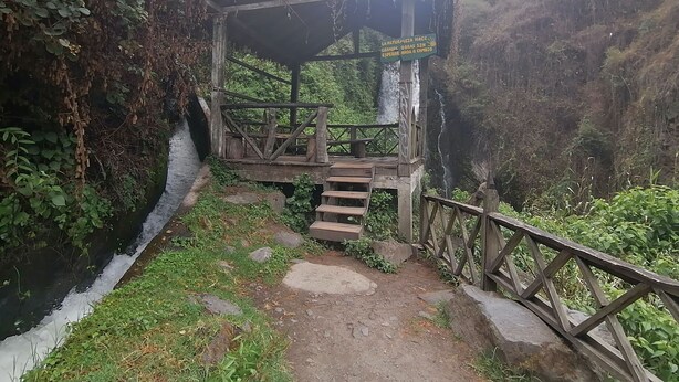 A wooden observation deck with a sign, surrounded by greenery and a rocky path. - Hostal y Complejo recreacional La Playita de Monse (Otavalo)