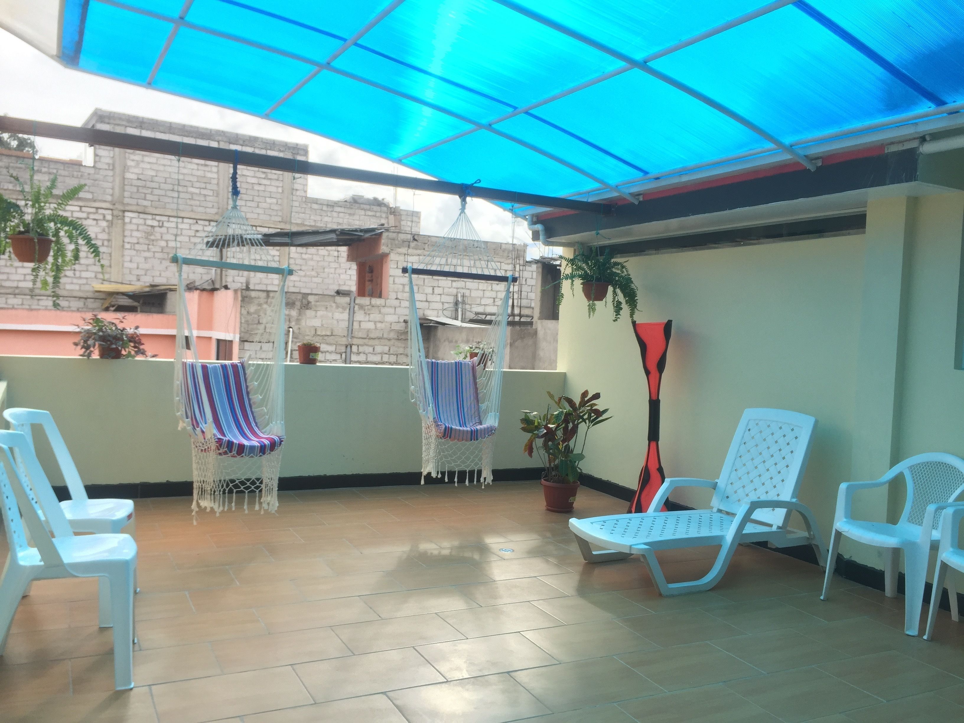 A covered patio area with hanging chairs, potted plants, and white plastic chairs.