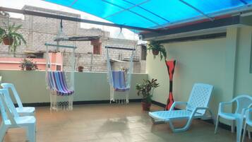 A covered patio area with hanging chairs, potted plants, and white plastic chairs.