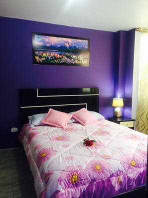 A bedroom with a bed, a nightstand, a lamp, and a wall-mounted picture.