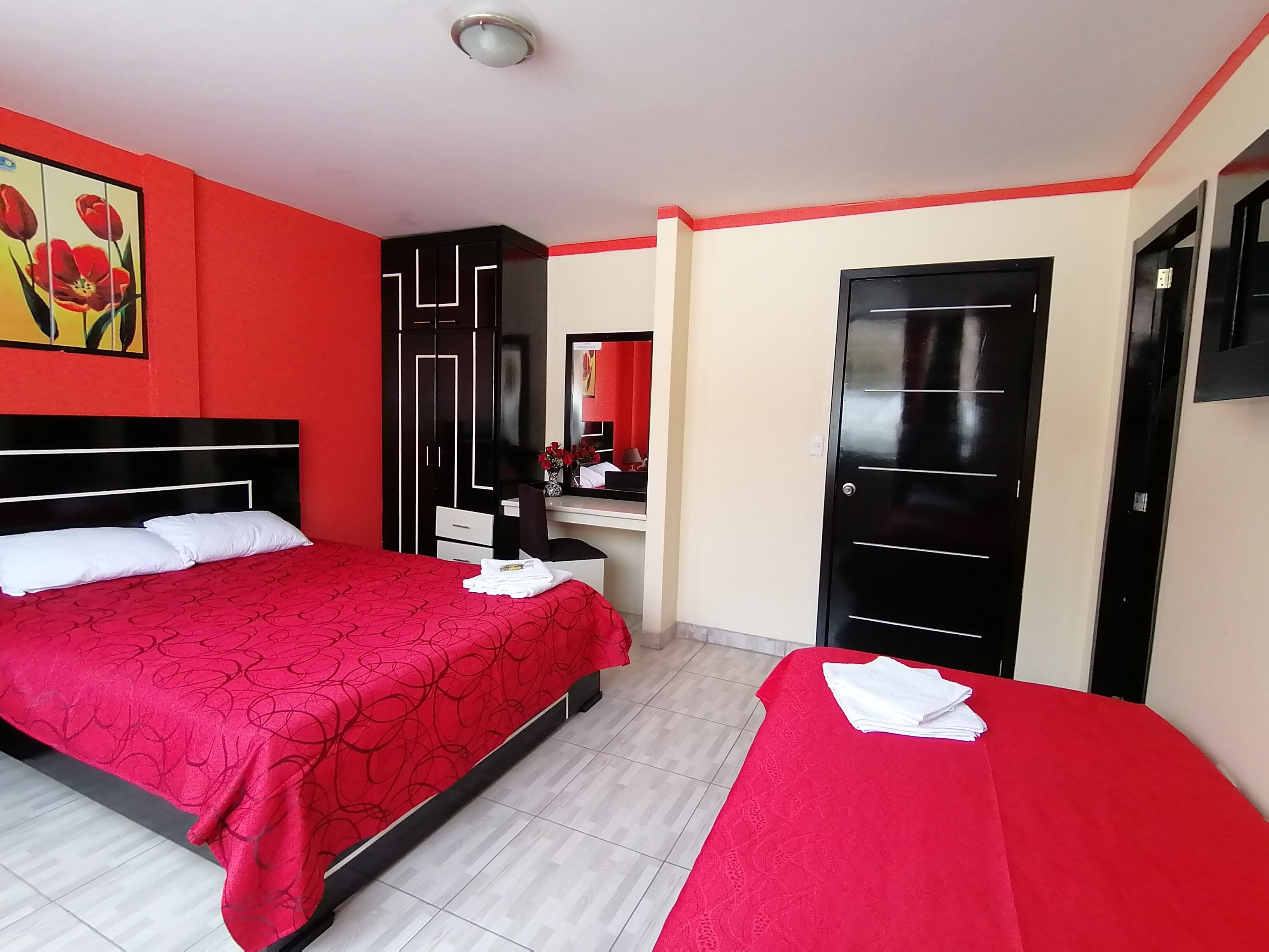 Habitación de hotel con dos camas, tocador con espejo y una decoración en colores rojo y negro.