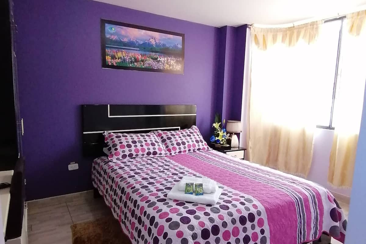 Un dormitorio con cama, un cuadro en la pared y una ventana con cortinas.