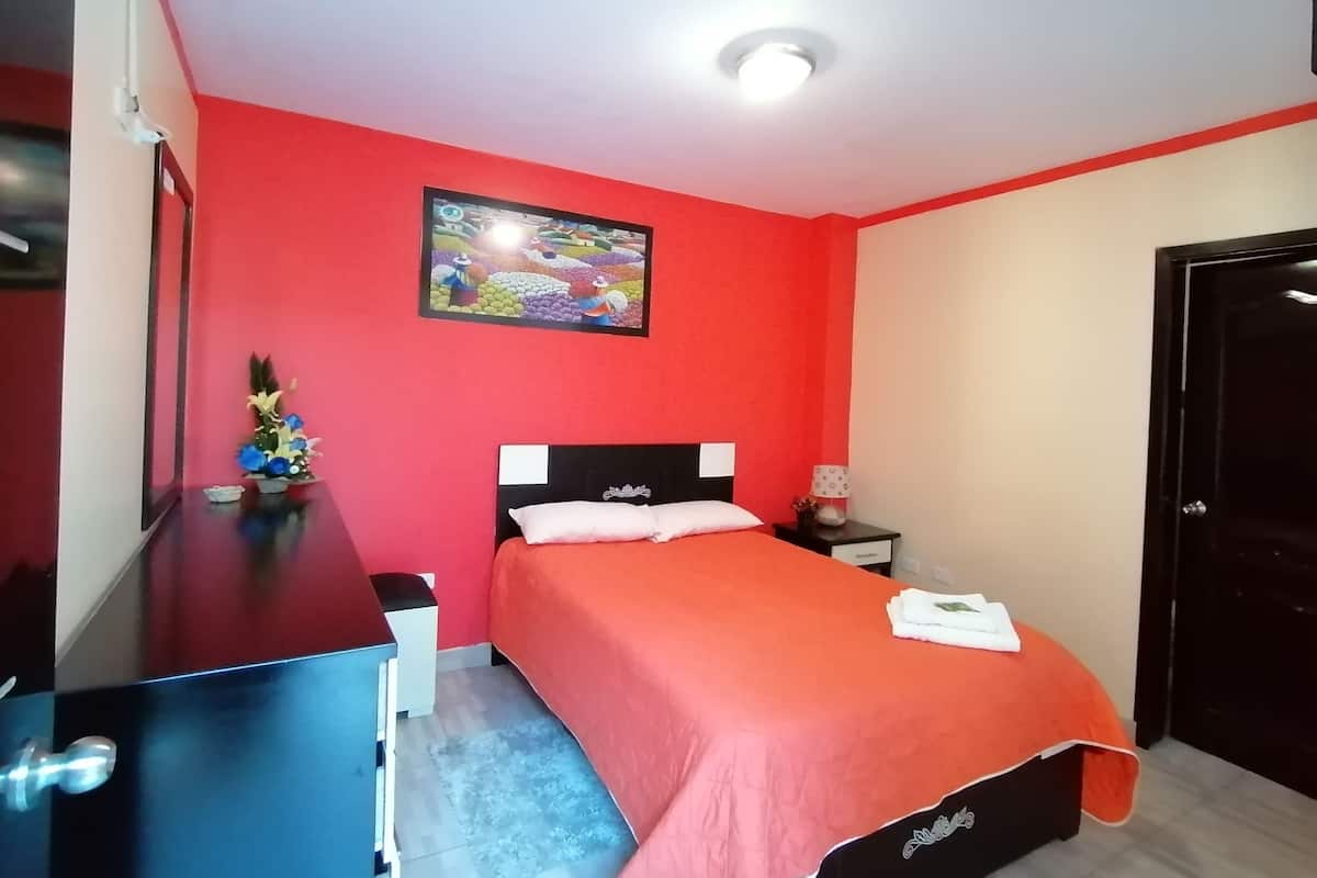 Una habitación con cama, escritorio, silla, mesita de noche y un cuadro colgado en la pared.
