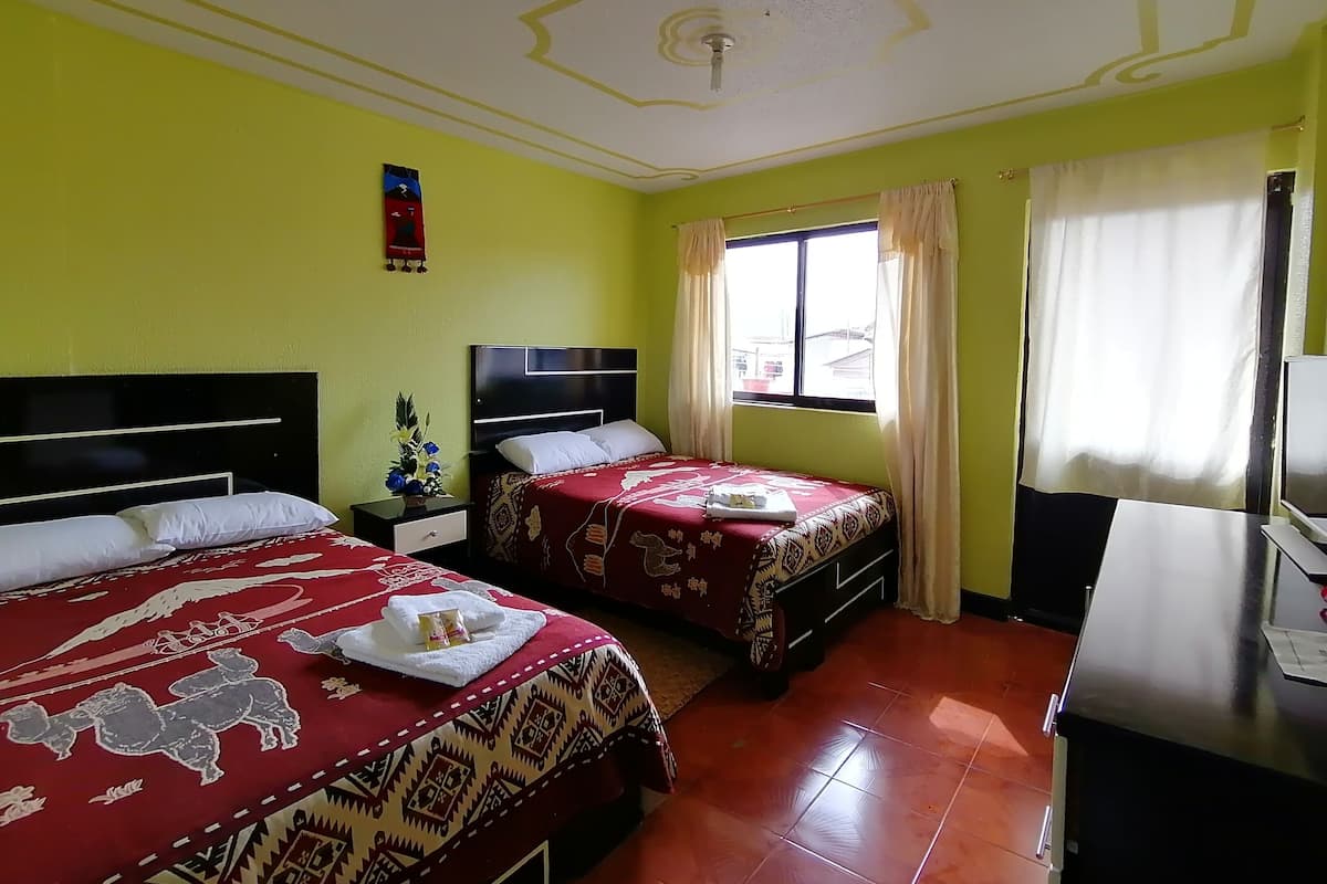 Habitación de hotel con dos camas, un escritorio, un televisor y una ventana con cortinas.