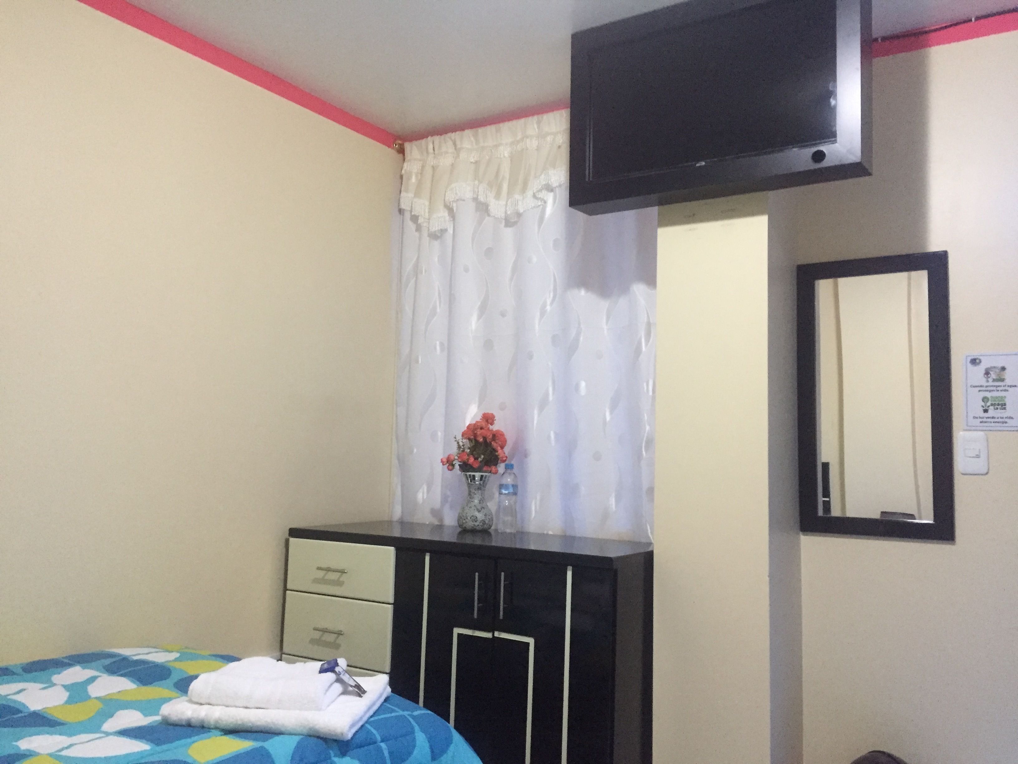 A bedroom with a bed, a dresser, a mirror, a TV, and a window with curtains.
