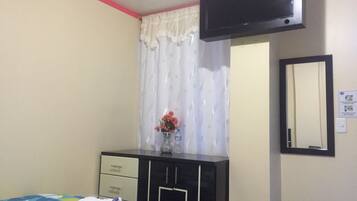 A bedroom with a bed, a dresser, a mirror, a TV, and a window with curtains.