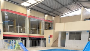 An indoor swimming pool with two slides, a covered roof, and a view of the outside building. - Hostal y Complejo recreacional La Playita de Monse (Otavalo)