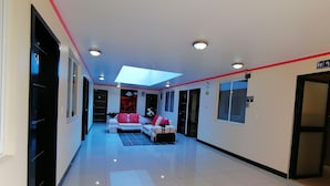 A hallway with a sofa and a coffee table, a skylight, and a sign indicating a bathroom. - Hostal y Complejo recreacional La Playita de Monse (Otavalo)