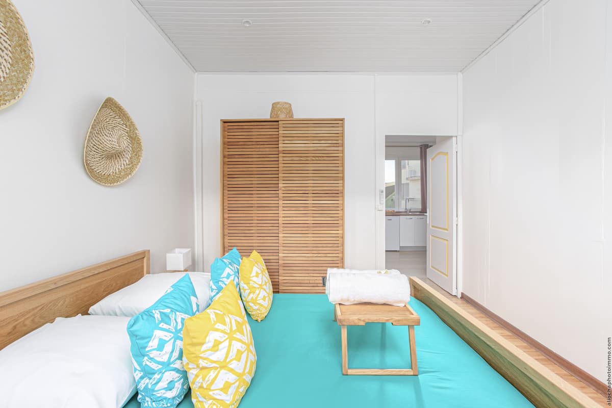A bedroom with a bed, pillows, a wooden bedside table, a wardrobe, and a bathroom visible through an open door.