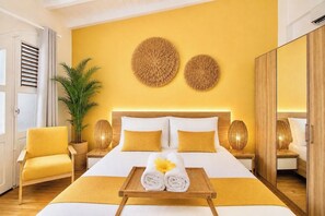 A hotel room with a bed, a chair, a plant, and decorative wall art. - Foyal Suites (Fort-de-France)