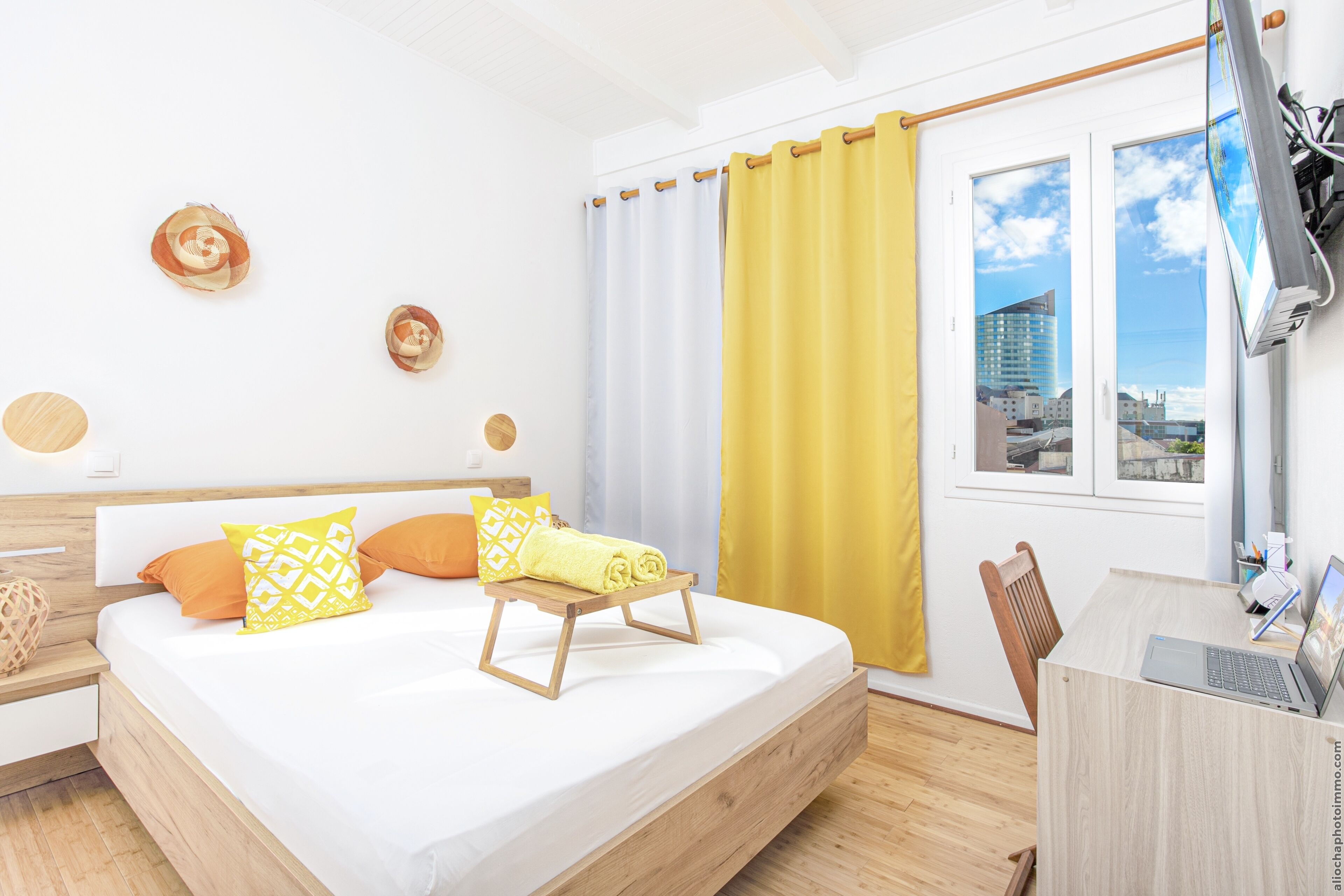 A modern bedroom with a bed, a desk, and a view of the city through a window.
