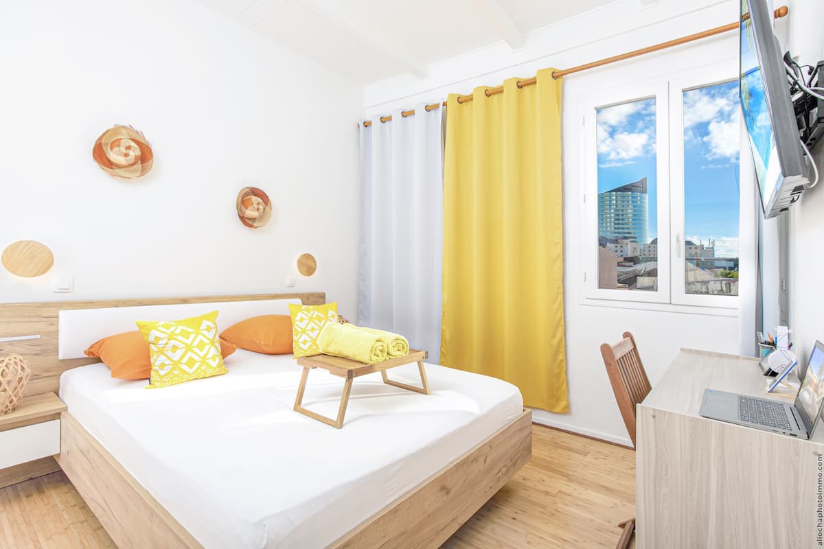 A modern bedroom with a bed, a desk, and a view of the city through a window.