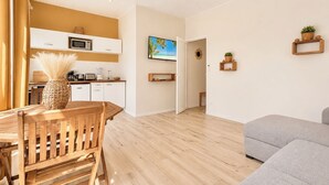 A modern kitchen with white cabinets, a microwave, and a dining area with a wooden table and chairs. - Foyal Suites (Fort-de-France)