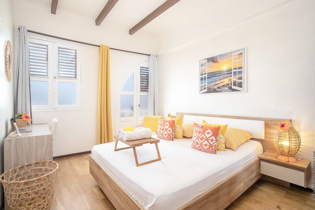 A bedroom with a bed, bedside table, lamp, and a view of the outside.