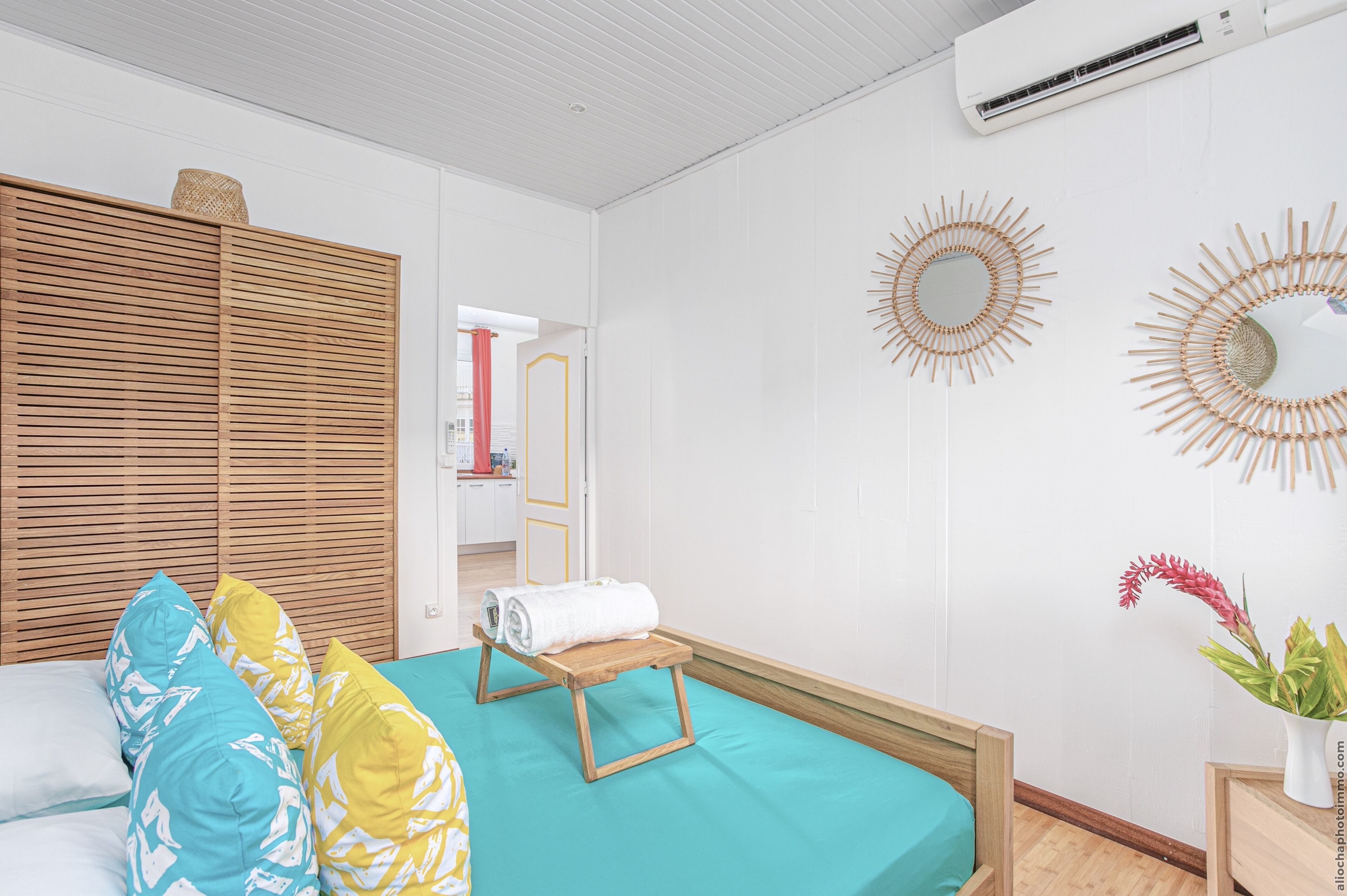 Un dormitorio con cama, armario de madera, espejo y una mesita con una toalla.