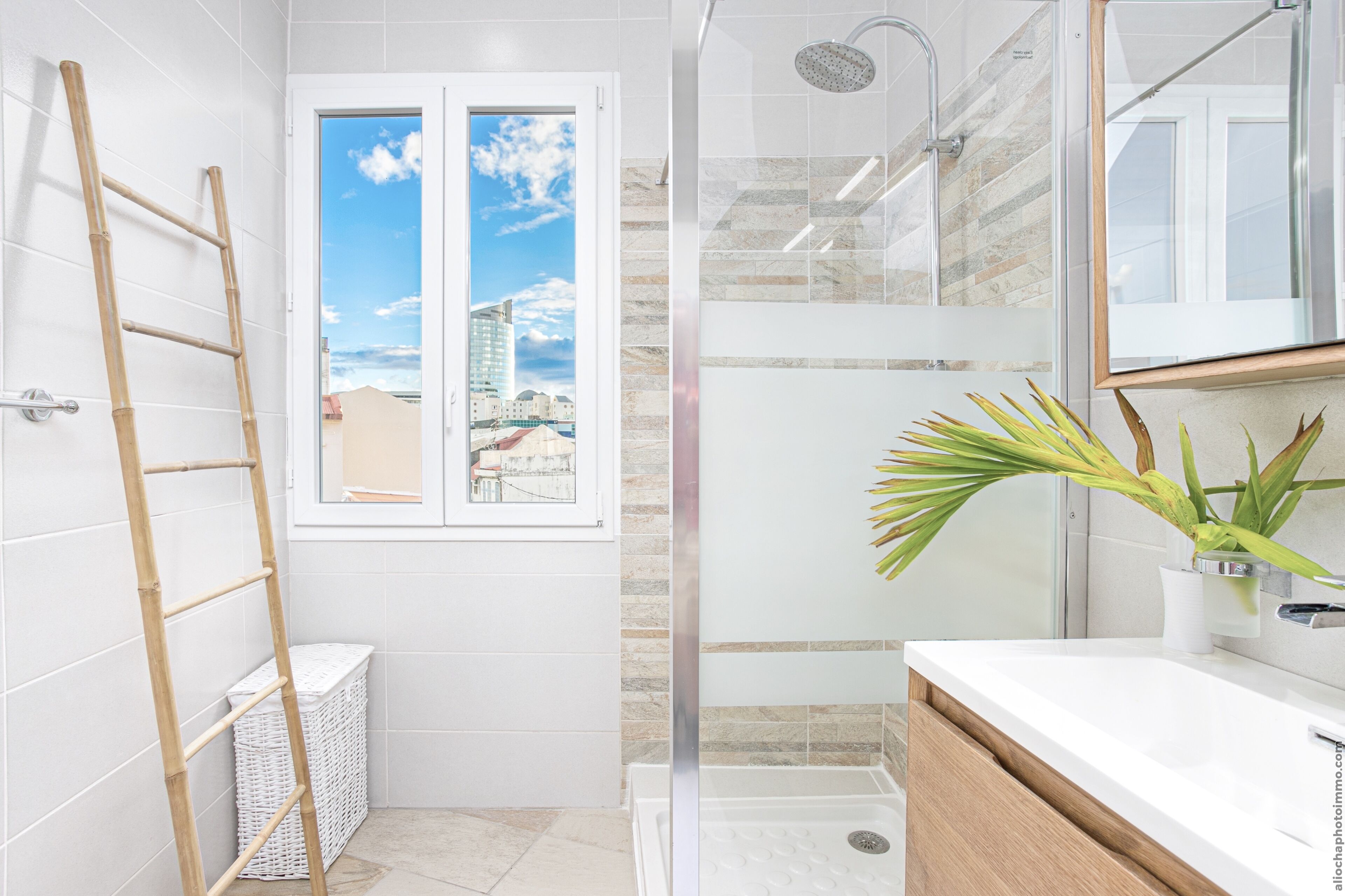 A bathroom with a shower, a window with a city view, a wooden ladder, and a potted plant.