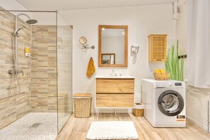 A modern bathroom with a glass-enclosed shower, a wooden vanity, a washing machine, and a mirror. - Foyal Suites (Fort-de-France)