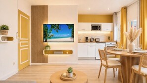 A modern kitchen with a flat-screen TV, wooden cabinets, and a dining area with a round table and chairs. - Foyal Suites (Fort-de-France)