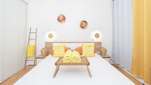 A hotel room with a bed, a bedside table, a lamp, a tray with towels, and a window with curtains. - Foyal Suites (Fort-de-France)