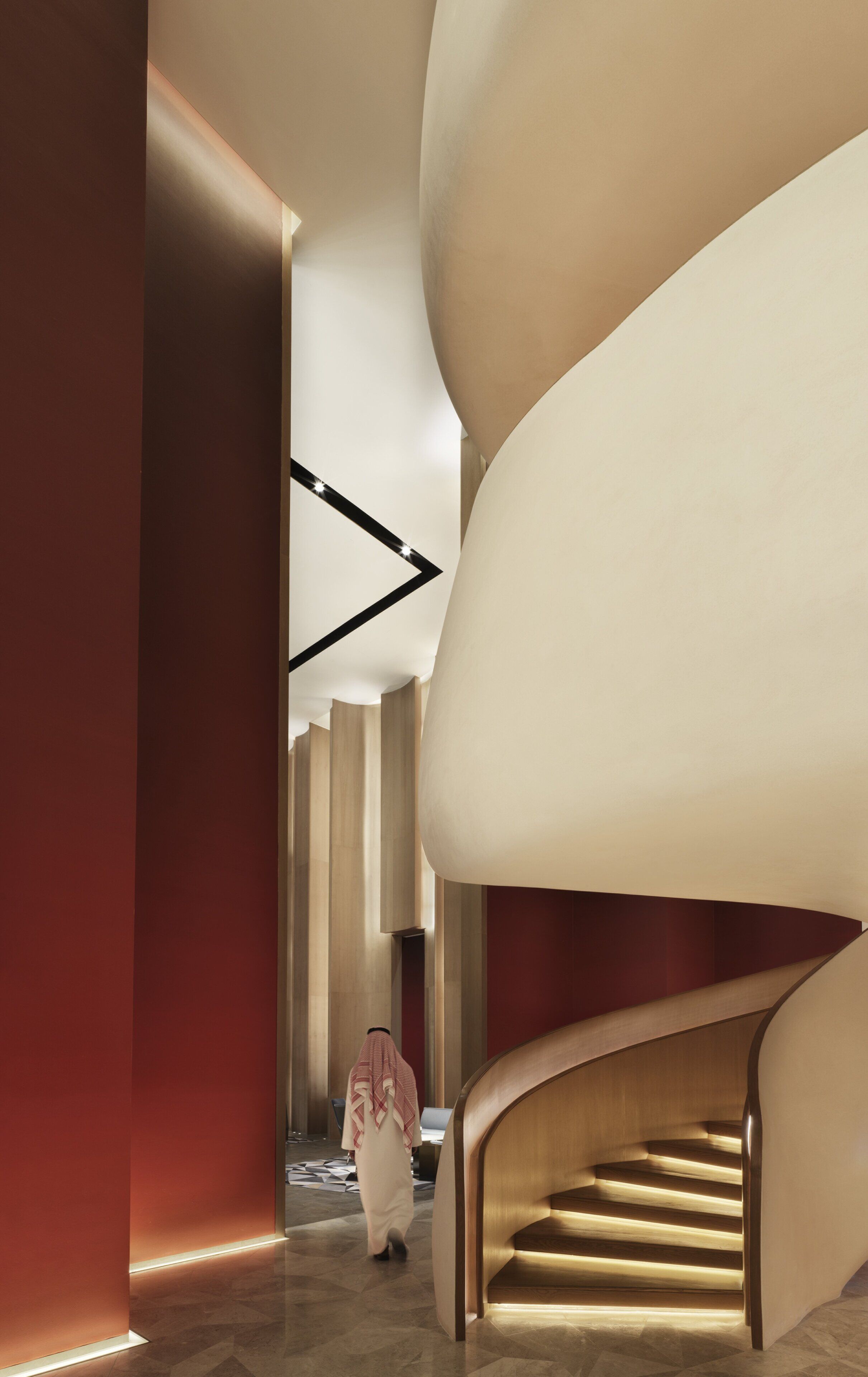 A modern interior with a curved staircase and a person walking down a hallway.