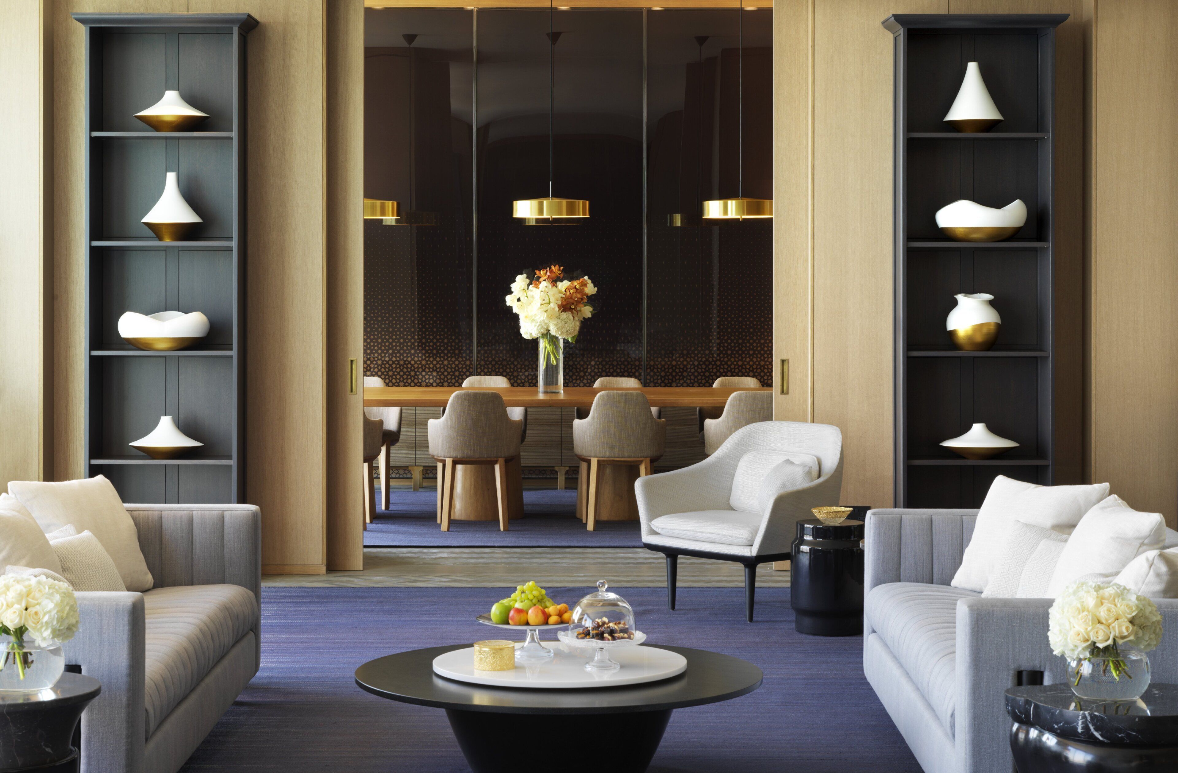 A modern hotel lobby with a dining area, sofas, and a coffee table with fruit and a vase.