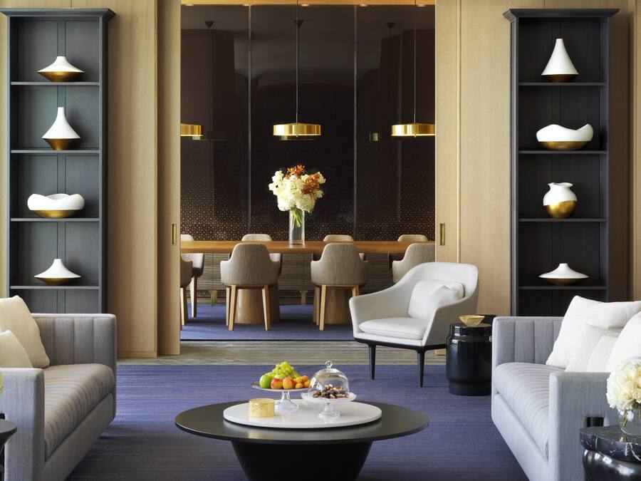 A modern hotel lobby with a dining area, sofas, and a coffee table with fruit and a vase.