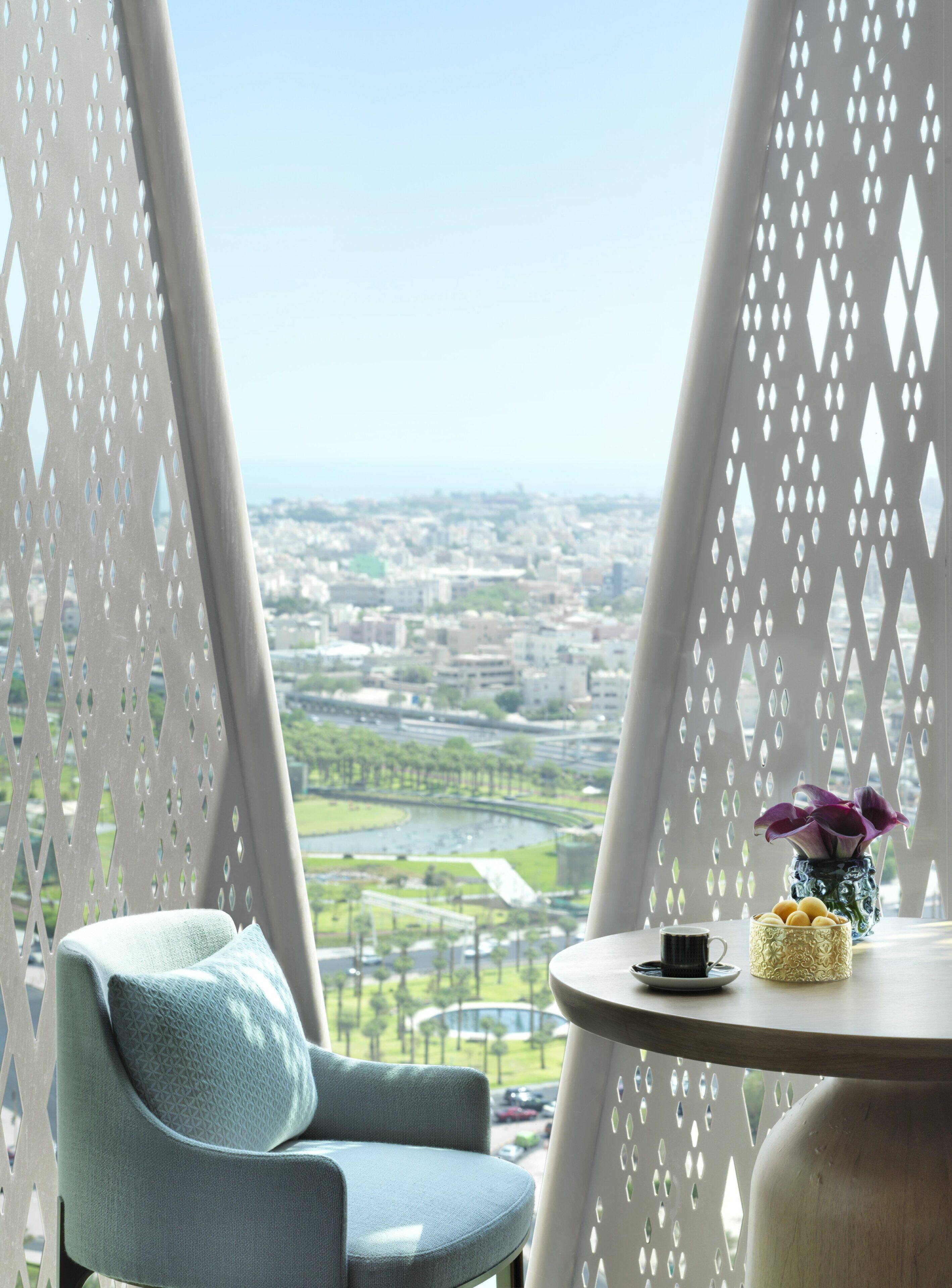 A balcony with a view of a cityscape, a chair, a table with a vase and a cup.