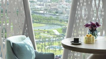 A balcony with a view of a cityscape, a chair, a table with a vase and a cup.
