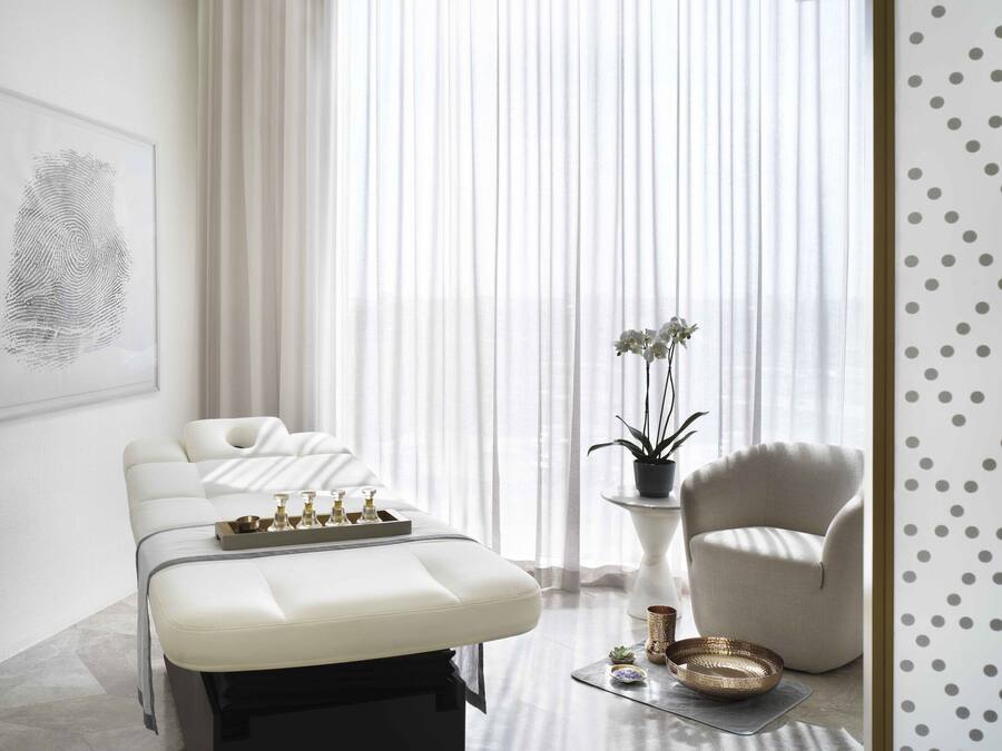 A spa room with a massage table, a chair, a small table with a plant, and a wall-mounted artwork.