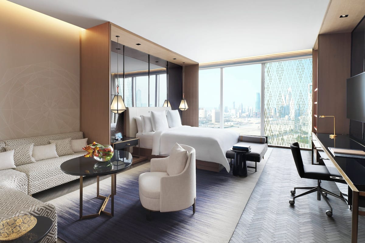 Une chambre d’hôtel moderne dotée d’un grand lit, d’un canapé, d’un bureau et offrant une vue sur le paysage urbain.
