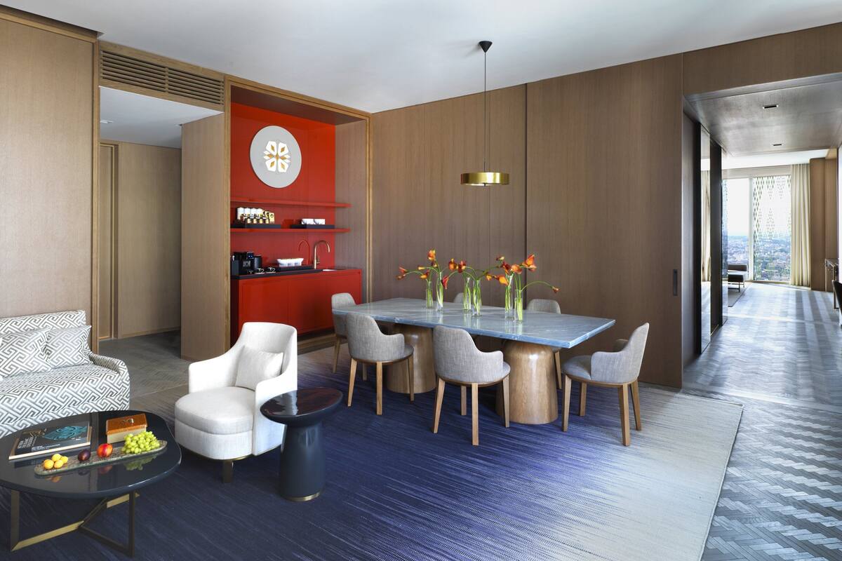Une chambre d’hôtel moderne avec un coin repas, un canapé, une table basse avec des fruits et une vue sur la ville.