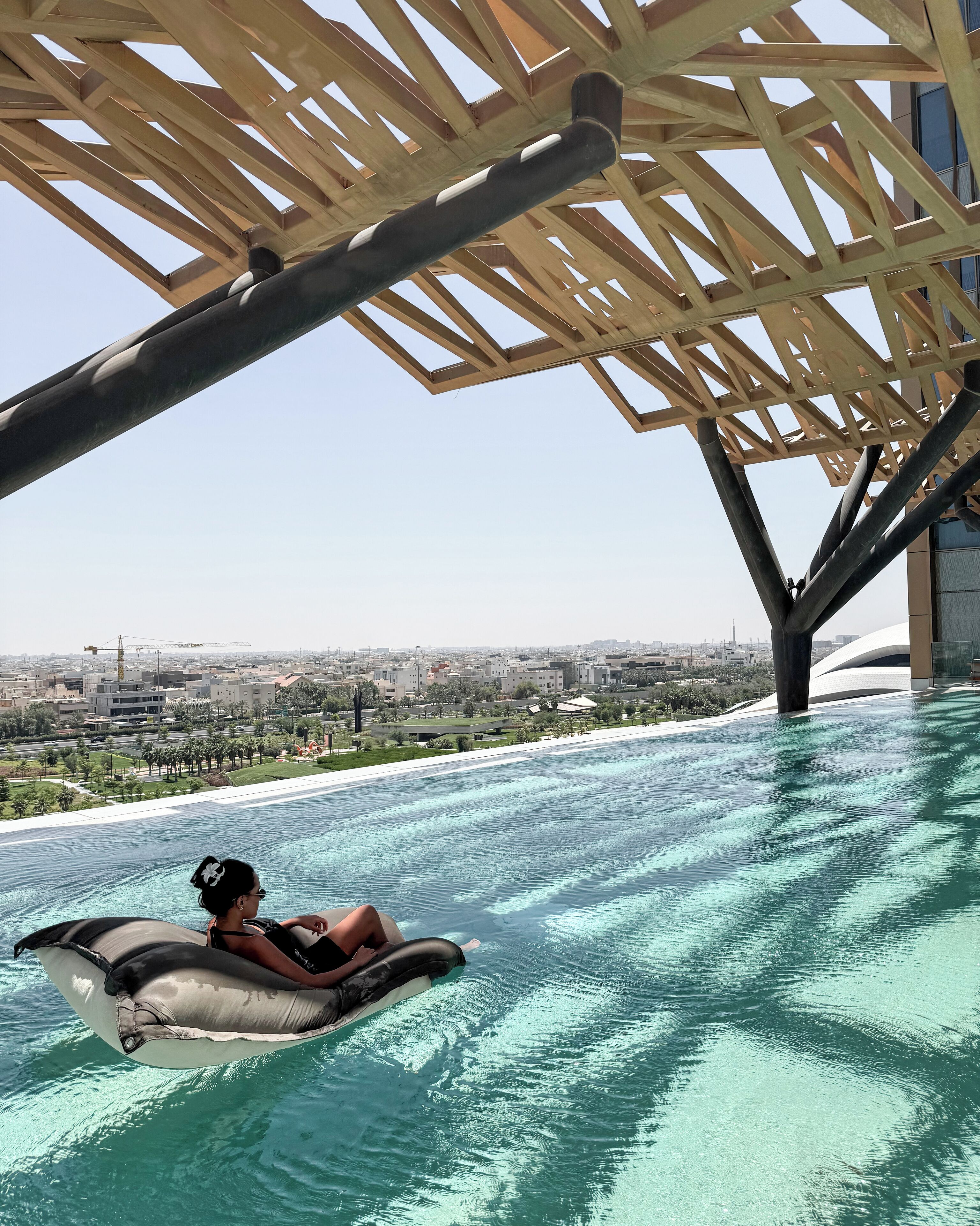 Una persona flota sobre un flotador en una piscina transparente con vistas a la ciudad.