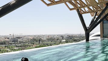 Una persona flota sobre un flotador en una piscina transparente con vistas a la ciudad.