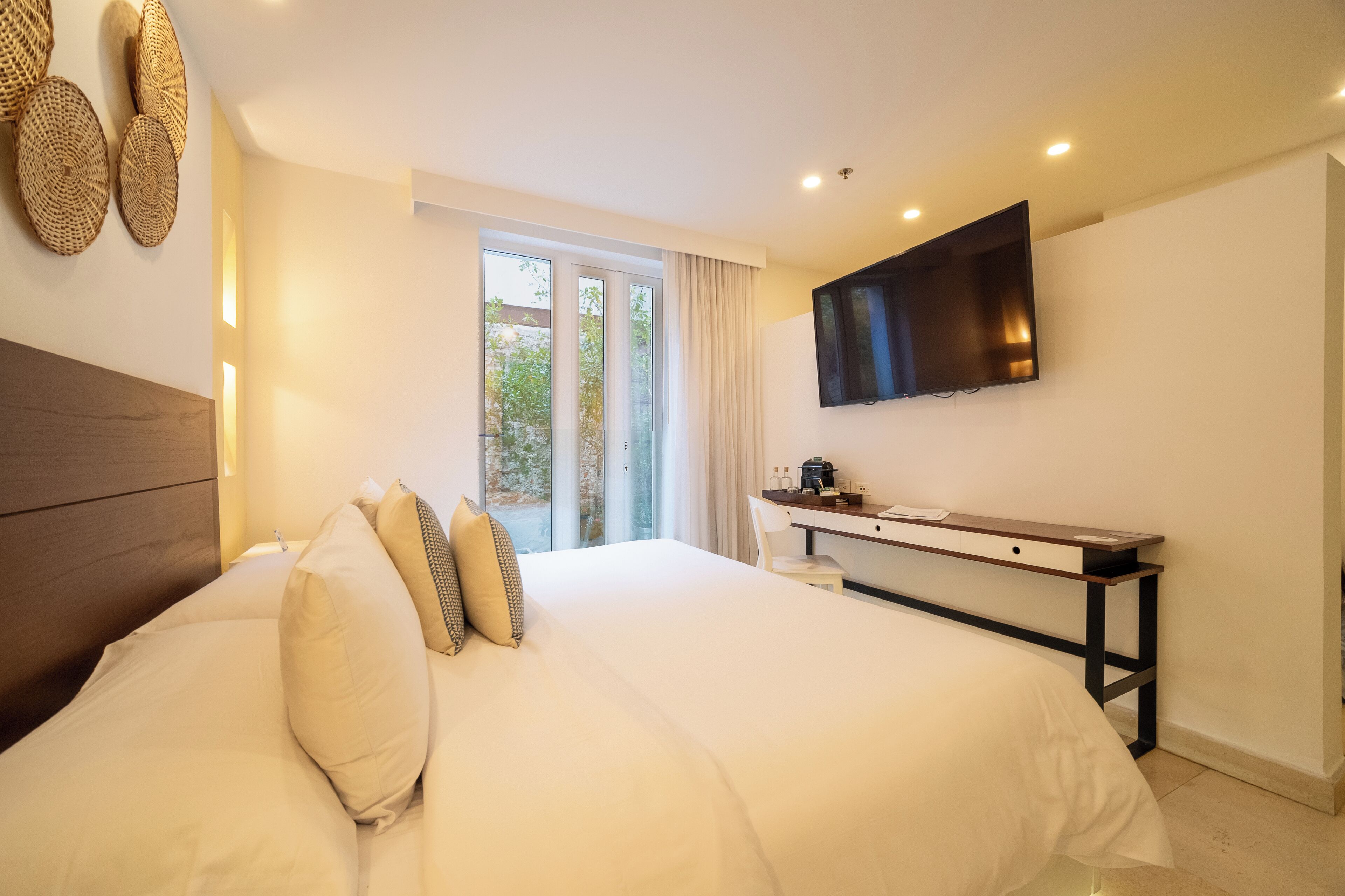 A bedroom with a large bed, a desk, a flat-screen TV, and a window with curtains.
