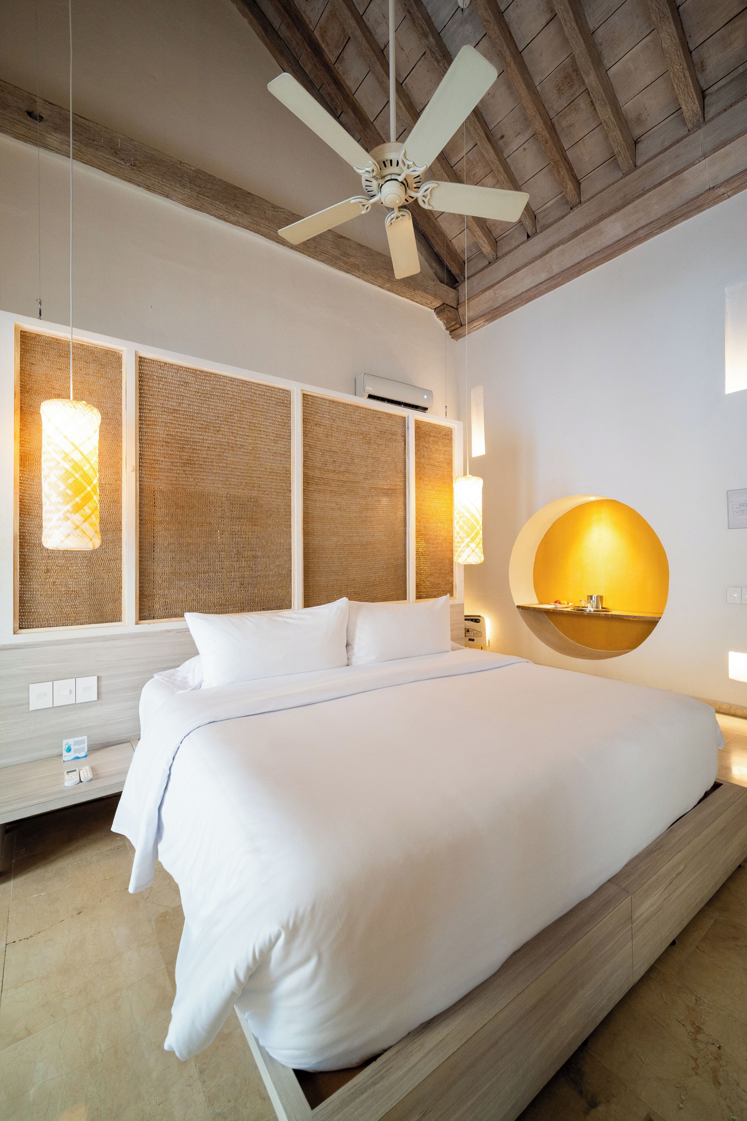 A modern hotel room with a large bed, a ceiling fan, and a round mirror.