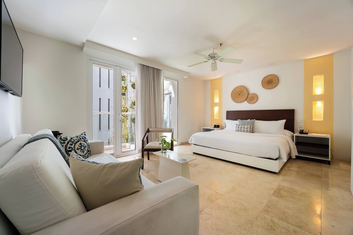 Una habitación de hotel moderna con cama, sofá, sillón, mesita y ventilador de techo.