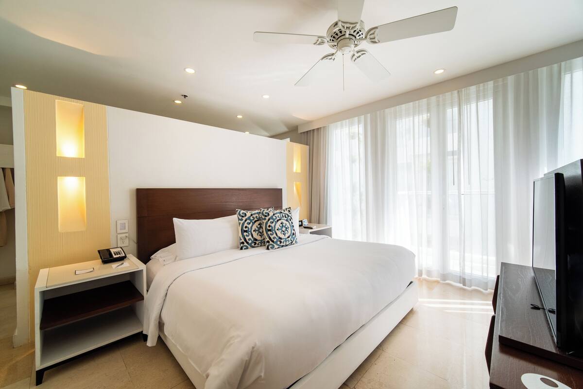 Una habitación de hotel moderna con una cama grande, un ventilador de techo, una mesita de noche con un teléfono y un televisor.