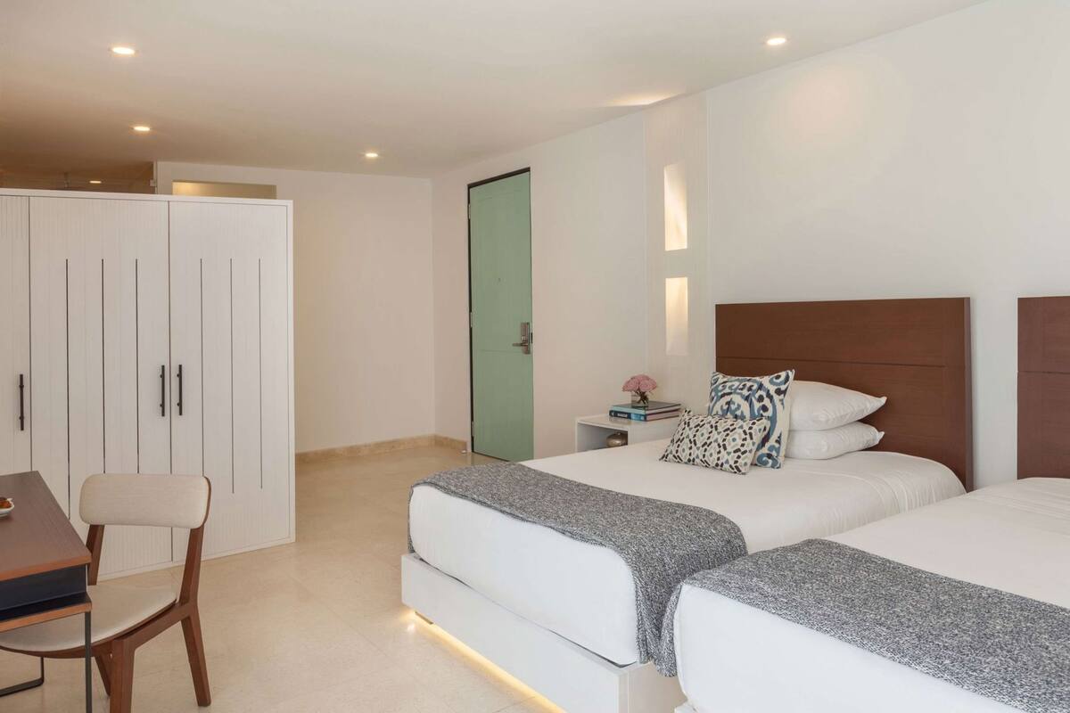 Habitación de hotel con dos camas, un escritorio, una silla, un armario y una puerta.