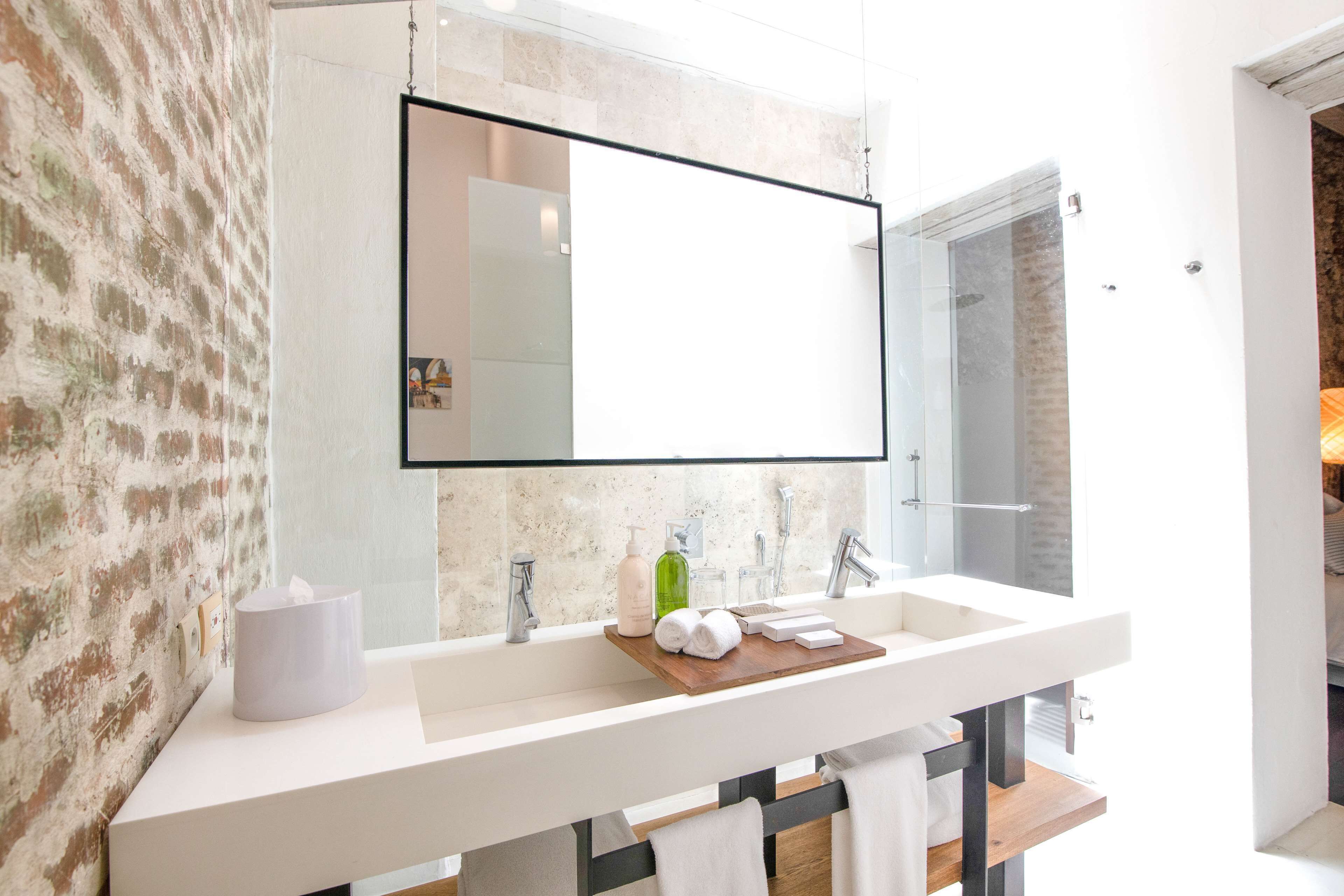 Un baño moderno con un espejo grande, lavamanos blanco y una bandeja de madera con toallas.