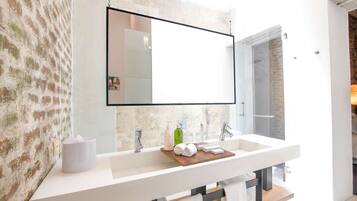 Un baño moderno con un espejo grande, lavamanos blanco y una bandeja de madera con toallas.