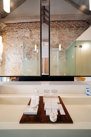 Experience a comfortable and inviting atmosphere in this stylish room with a rustic brick accent wall, large mirror, and neatly arranged toiletries.