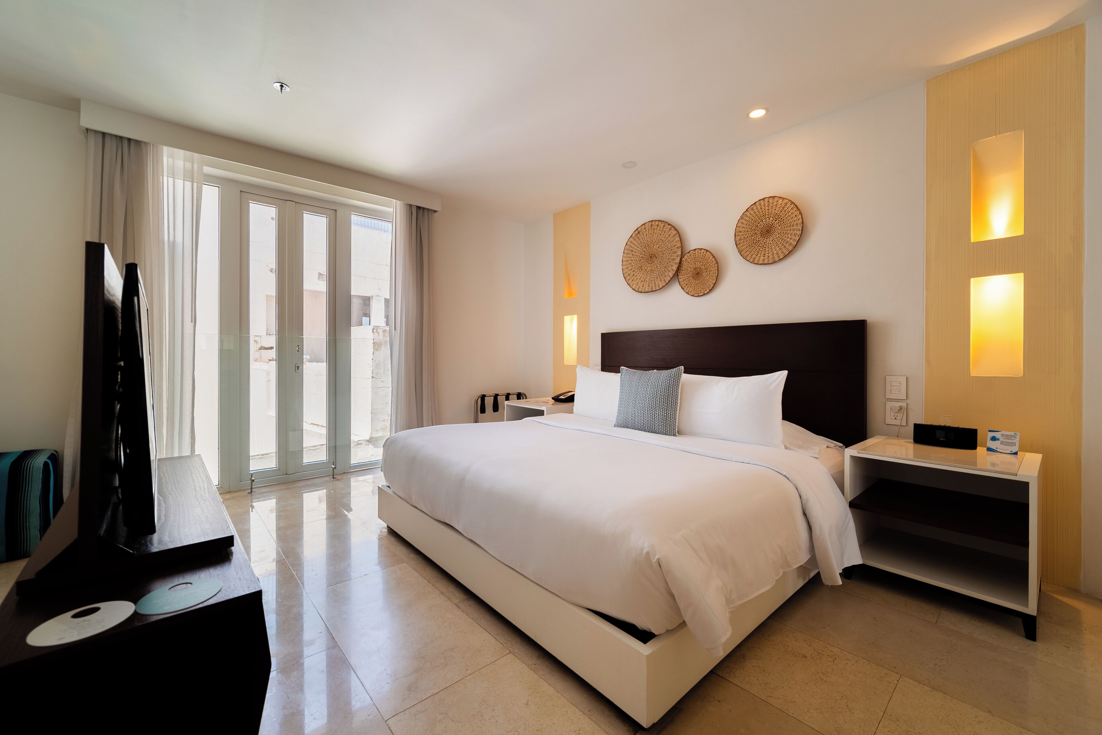 A modern hotel room with a large bed, a flat-screen TV, and a sliding glass door to the balcony.